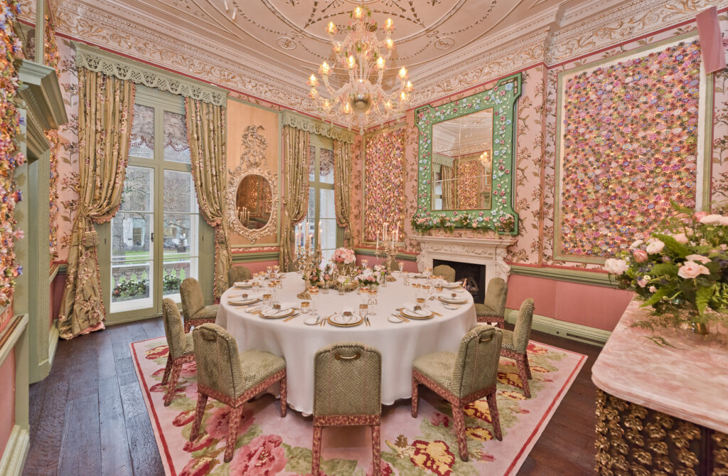 Luxury Wedding Venue Annabel's in London, designed for a formal dining experience. The space features floral-themed walls, ornate curtains, a round table set with fine china, a chandelier, and detailed ceiling work, perfect for hosting upscale events.