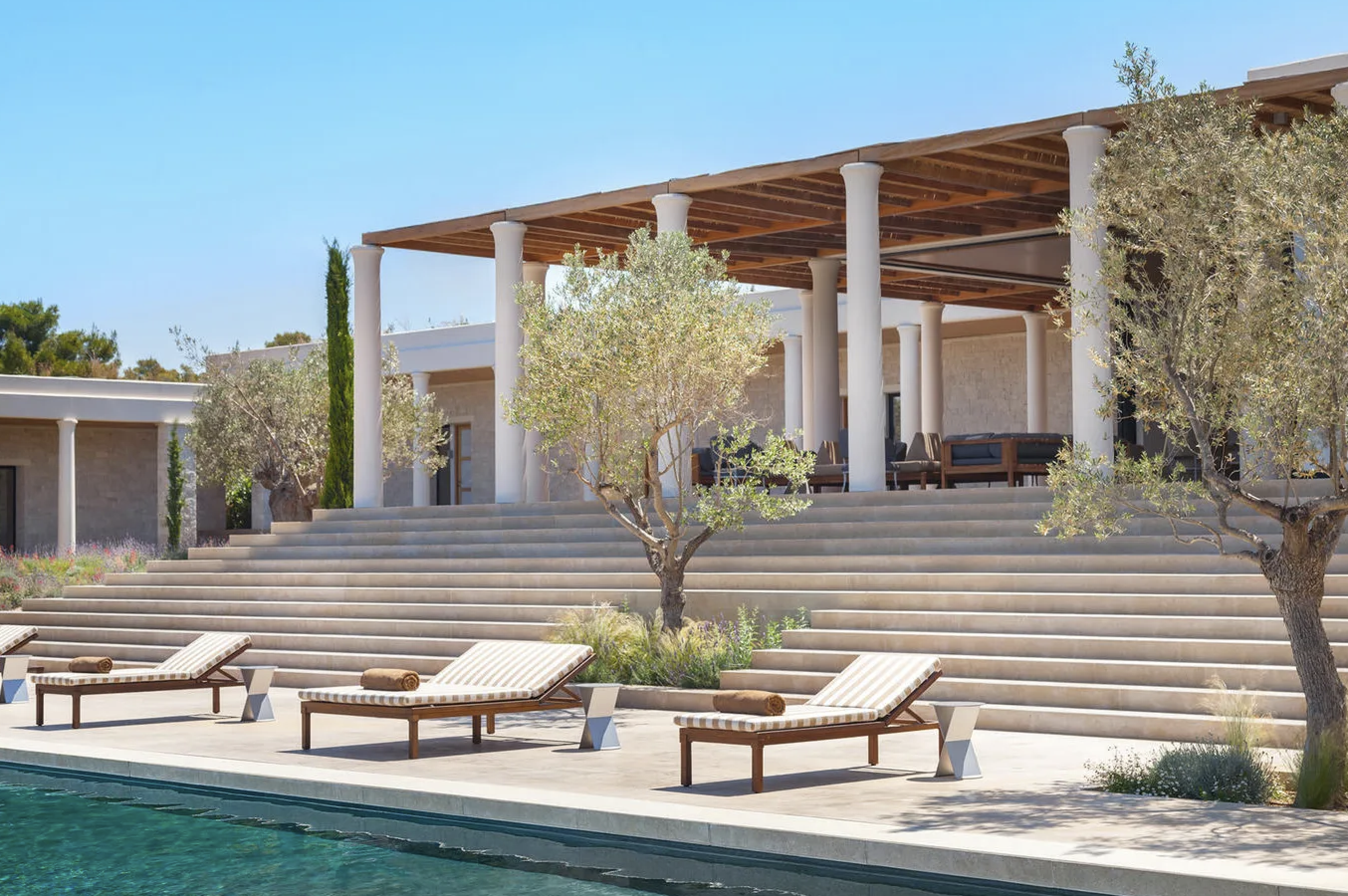 Amanzoe wedding venue in Greece featuring elegant white columns, stone steps, poolside loungers, and Mediterranean landscaping.